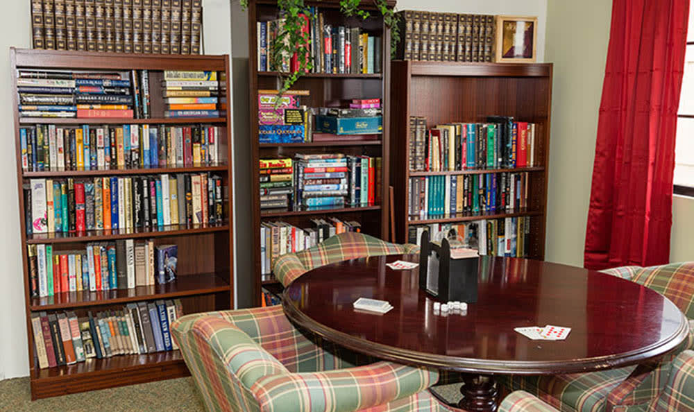 A cozy library corner with bookshelves filled with a variety of books and a round table surrounded by plaid armchairs.