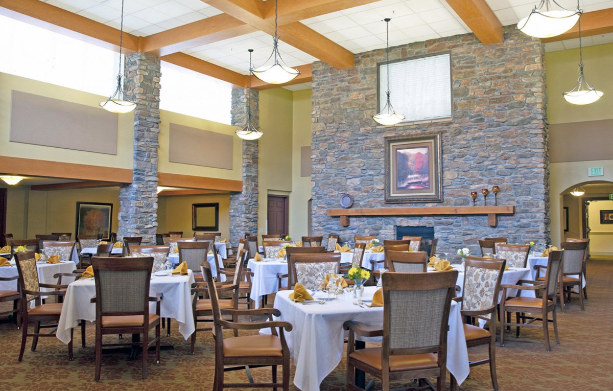 A well-decorated dining area with neatly arranged tables and chairs, featuring a stone fireplace and warm lighting.