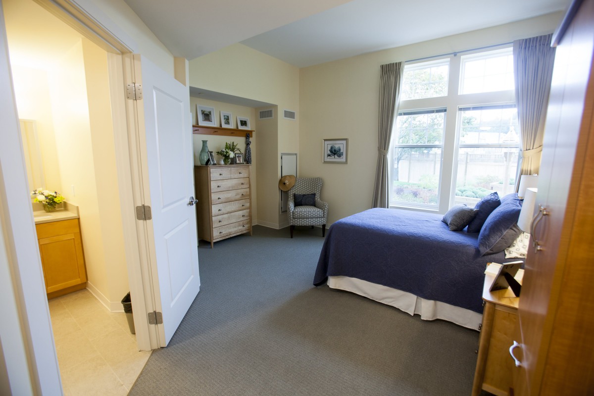 A cozy bedroom with a neatly made bed, large window, and dresser.