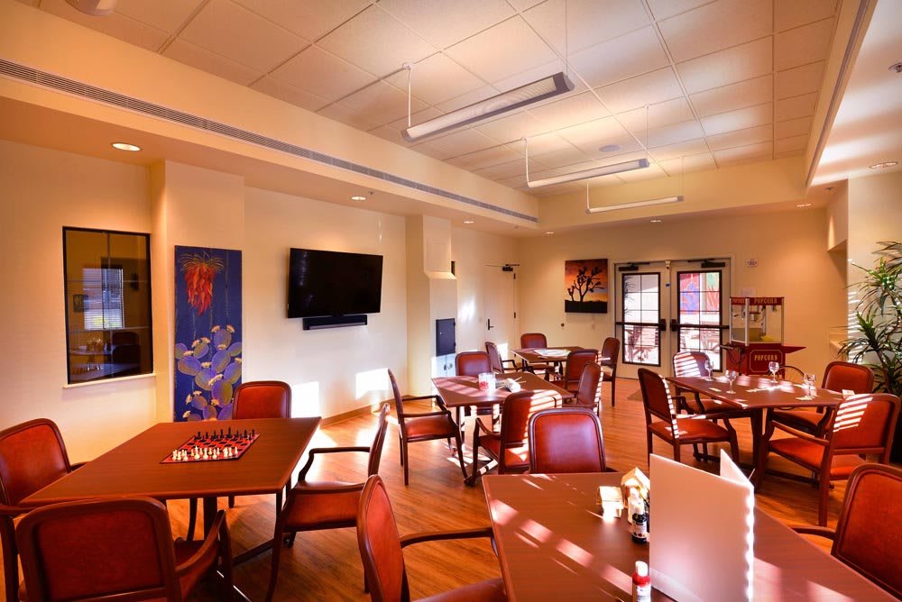 A well-lit dining room with multiple tables and chairs, featuring a wall-mounted television and decorative artwork.