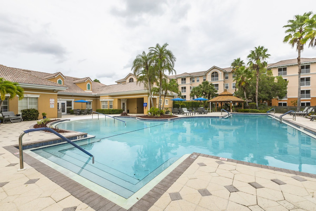 A luxurious outdoor swimming pool area surrounded by palm trees and resort buildings.