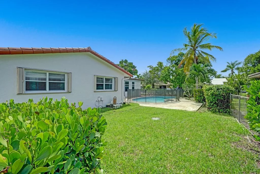 A beautiful house with a lush green lawn, a swimming pool, and palm trees under a clear blue sky.