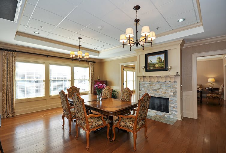 A beautifully designed dining room featuring a wooden table and ornate chairs, with a fireplace adorned with artwork and elegant chandeliers lighting the space.