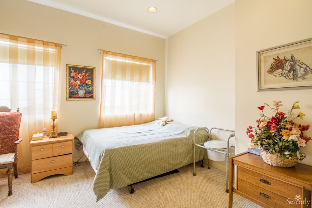 A cozy bedroom with a single bed, decorated with artwork and featuring a nightstand and chair by the window.