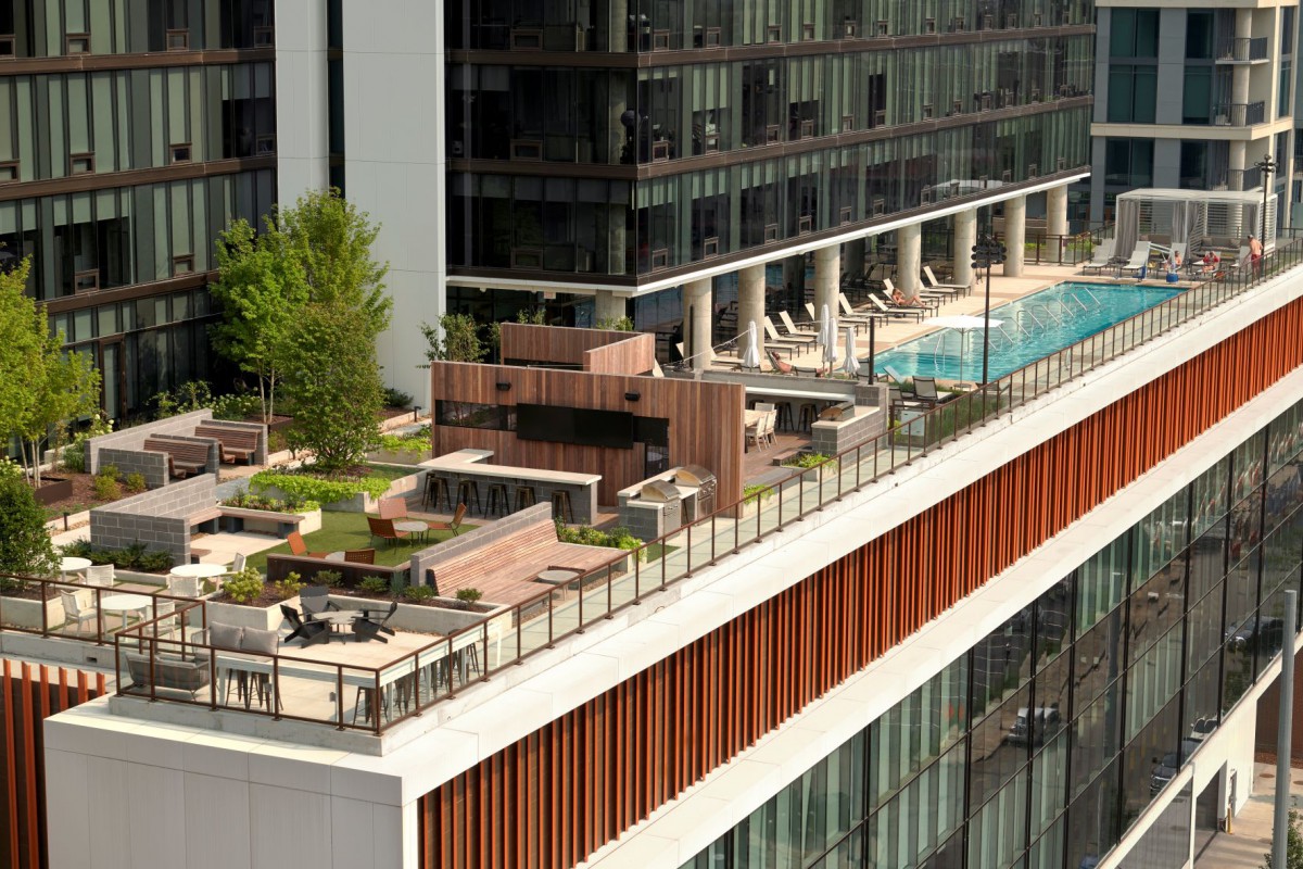 A modern rooftop featuring a pool, green spaces, and outdoor seating in an urban setting.