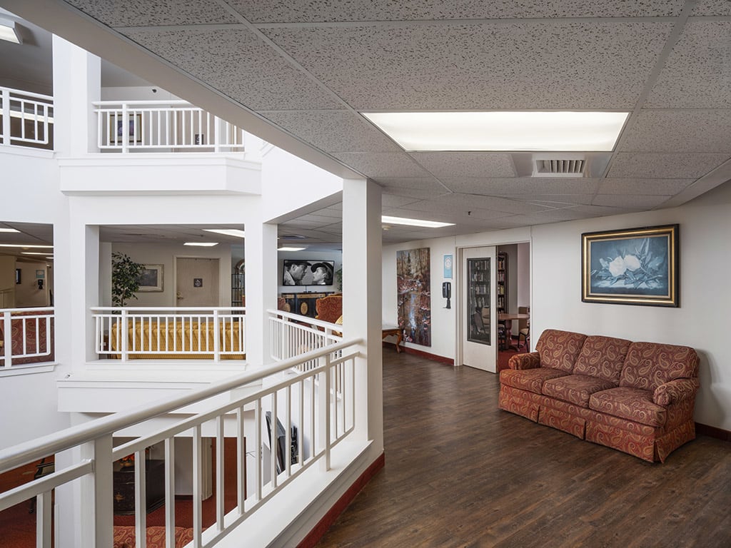 A modern interior hallway with seating and artwork, featuring wood flooring and railings.