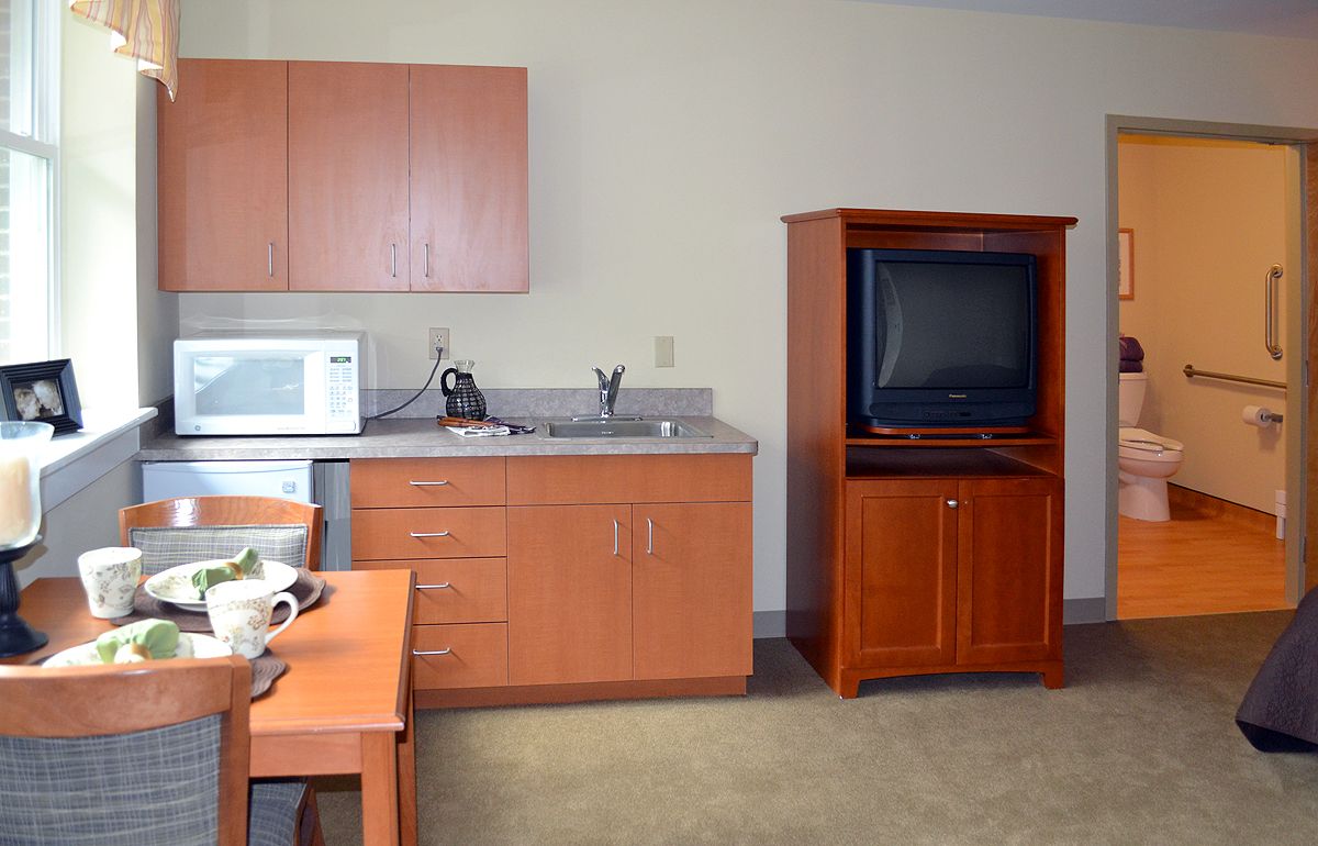A small kitchen area with wooden cabinets, a microwave, and a TV cabinet.