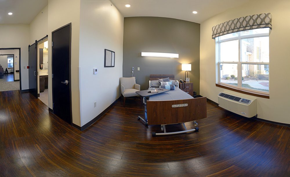 A modern hospital room featuring a patient bed, comfortable seating, and large windows providing natural light.