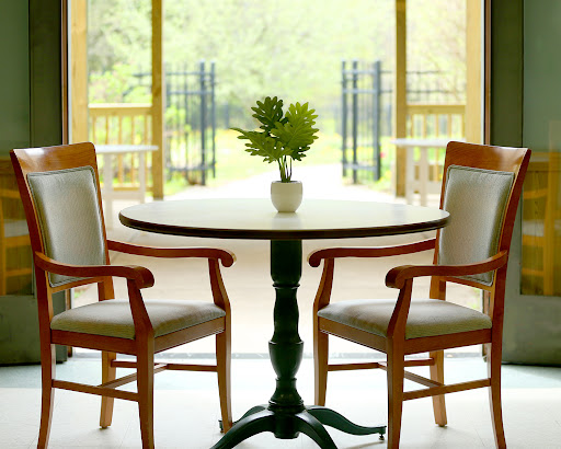 A cozy dining area with a round table, two wooden chairs, and a small potted plant, illuminated by natural light.