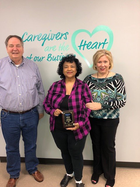 Three people standing together in front of a wall with motivational text, celebrating an award.