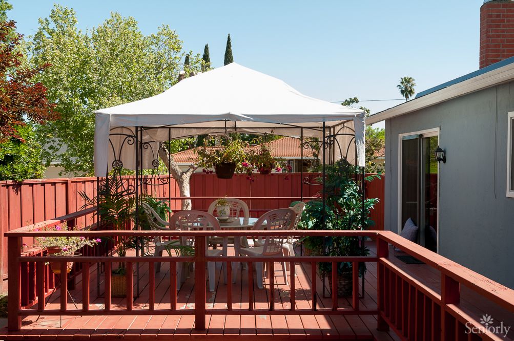 A cozy patio with a gazebo, surrounded by plants and outdoor furniture on a sunny day.