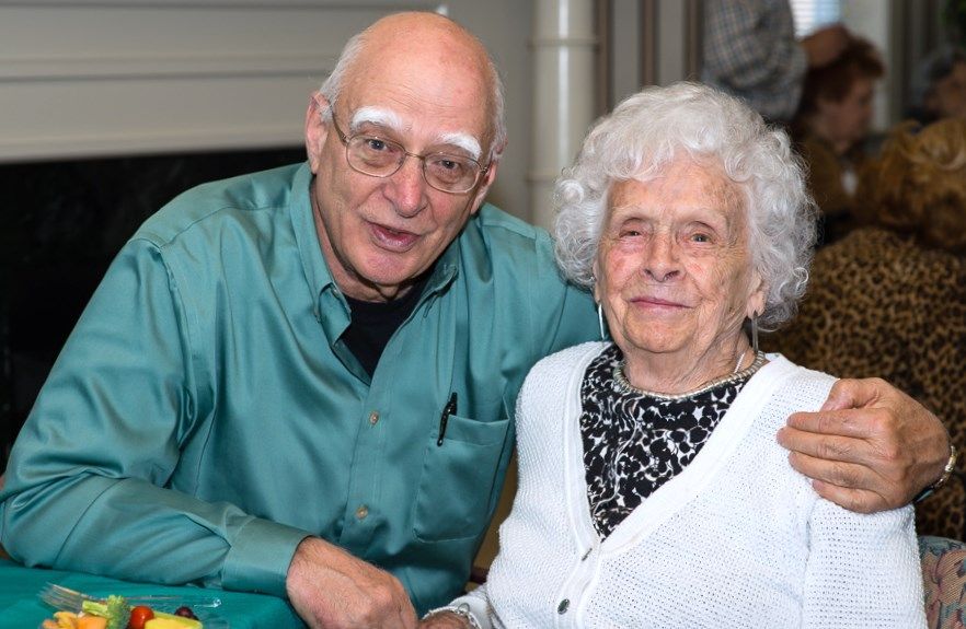 An elderly man and woman smiling while sitting together indoors.