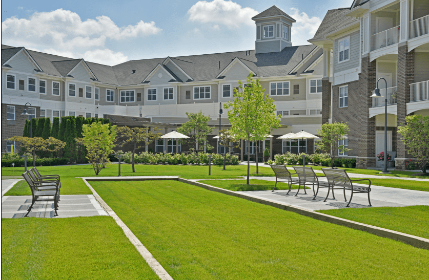 A well-maintained garden area in front of a large residential building with seating and umbrellas on a sunny day.