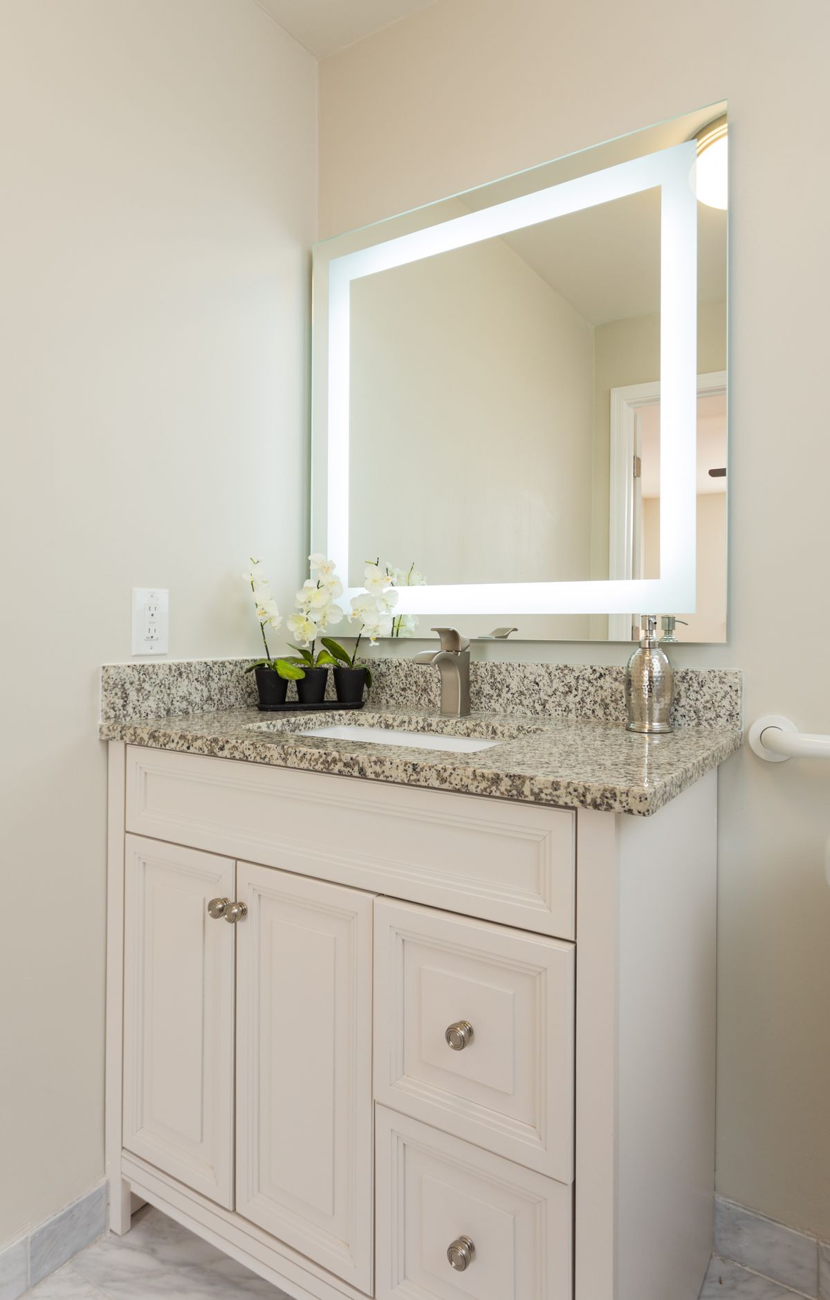 A modern bathroom vanity with a granite countertop and illuminated mirror.
