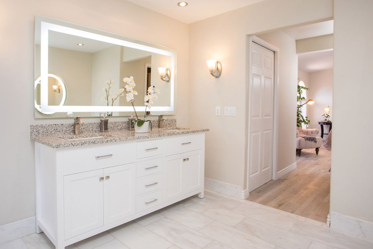 A modern bathroom featuring a large vanity with an illuminated mirror and elegant orchid decoration.