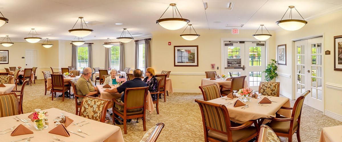 A cozy dining room with several tables and chairs, where people are enjoying a meal together.