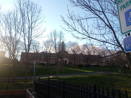 A serene view of a building surrounded by trees and an open park under a clear sky.
