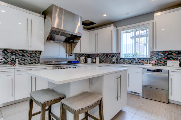 A modern kitchen featuring white cabinets, a central island with stools, and a stainless steel range hood.