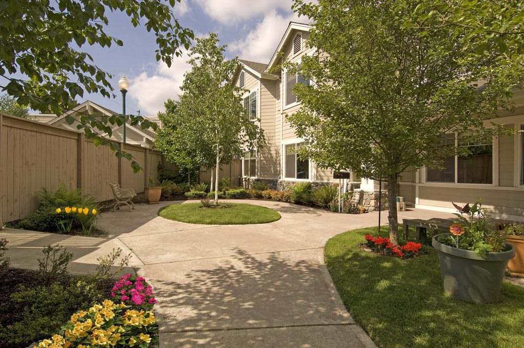 A well-maintained house with a driveway surrounded by trees and colorful flowers.