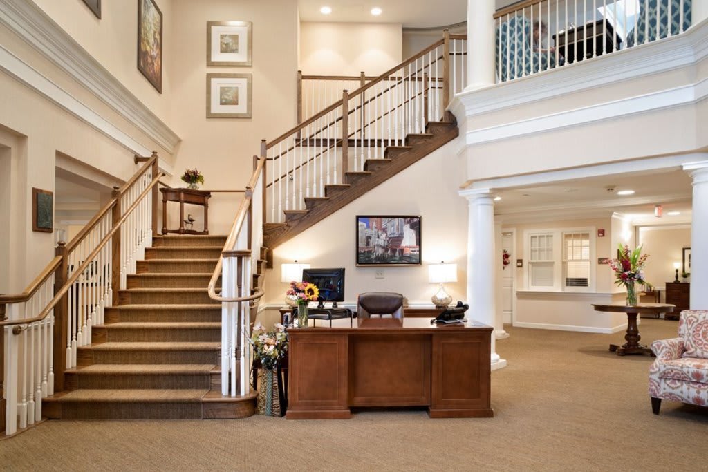 A spacious lobby with a grand staircase and a wooden reception desk.
