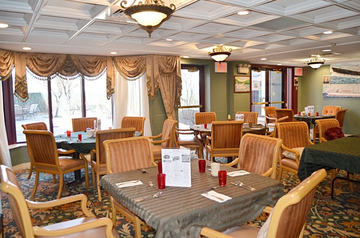 An elegant dining area with neatly arranged tables and chairs, decorated with chandeliers and drapes.