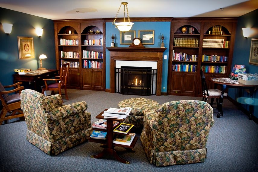 A cozy living room featuring a fireplace surrounded by filled bookshelves and two floral-patterned armchairs.