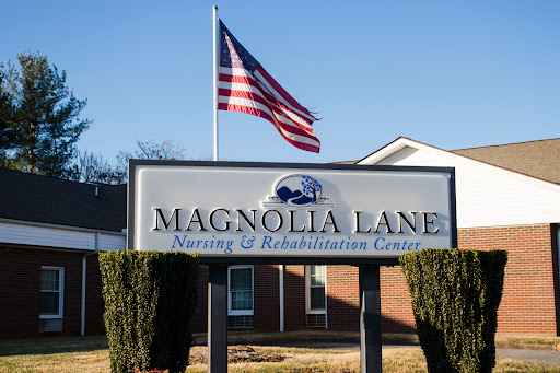 Entrance sign for Magnolia Lane Nursing & Rehabilitation Center, with an American flag waving in the background.