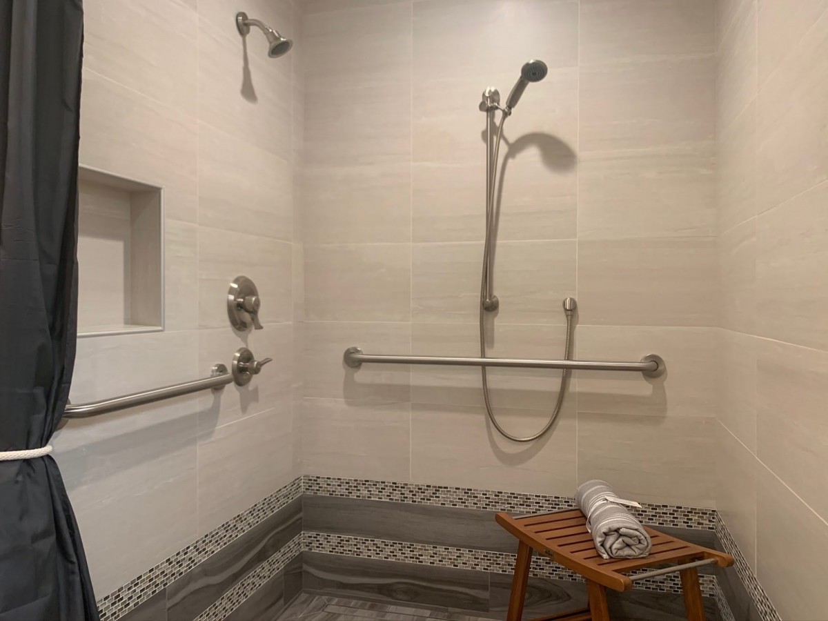 An accessible bathroom with a shower, grab bars, and a wooden bench.