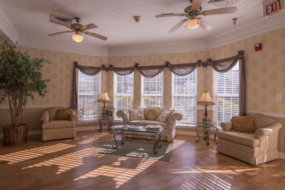 A cozy living room with large windows, comfortable sofas, and ceiling fans.