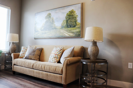 A cozy living room setting featuring a beige sofa adorned with decorative pillows, accompanied by an elegant lamp and a landscape painting.