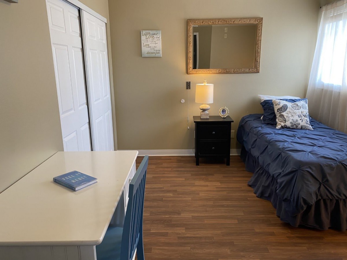 A cozy bedroom with a neatly made bed, nightstand, and mirror above.