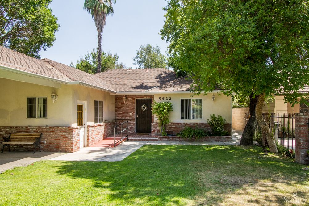 A charming single-story house with a green lawn and mature trees in the front yard.