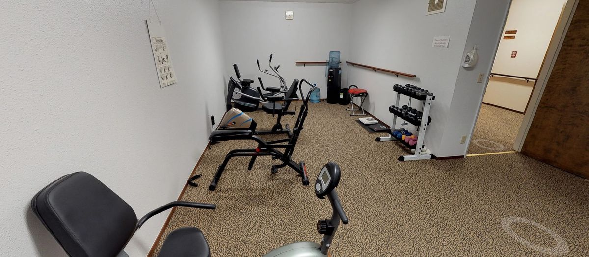 A small indoor gym with various exercise equipment including stationary bikes, a treadmill, and dumbbells.