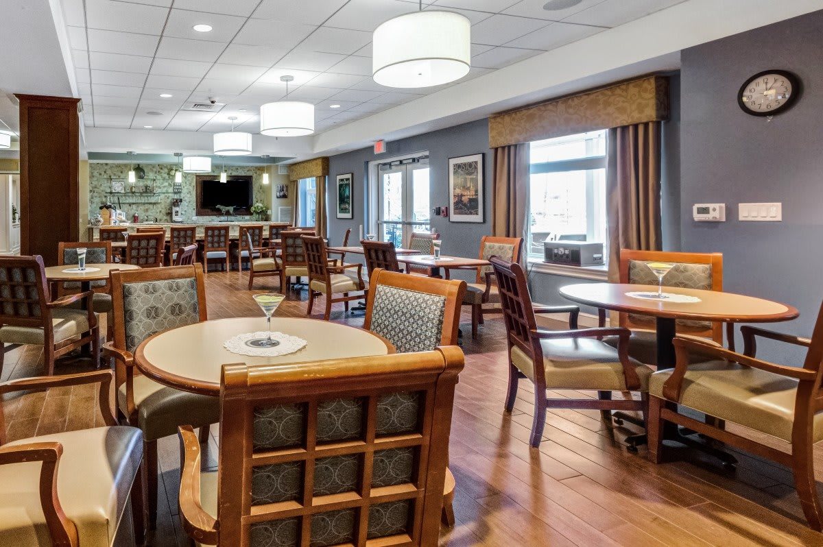 A well-lit dining area with wooden tables and chairs, featuring contemporary decor and large windows.