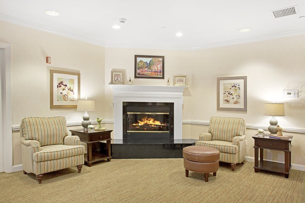 A cozy living room featuring a warm fireplace, surrounded by armchairs and artwork.