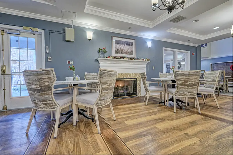 A cozy dining area with a fireplace, featuring wicker chairs and wooden tables on a polished wooden floor.
