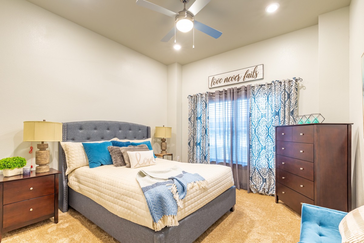 A well-decorated bedroom featuring a comfortable bed, stylish curtains, and a ceiling fan.