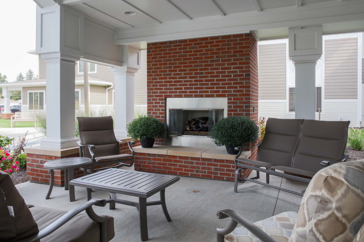 An inviting outdoor patio featuring a brick fireplace, comfortable seating, and lush potted plants.