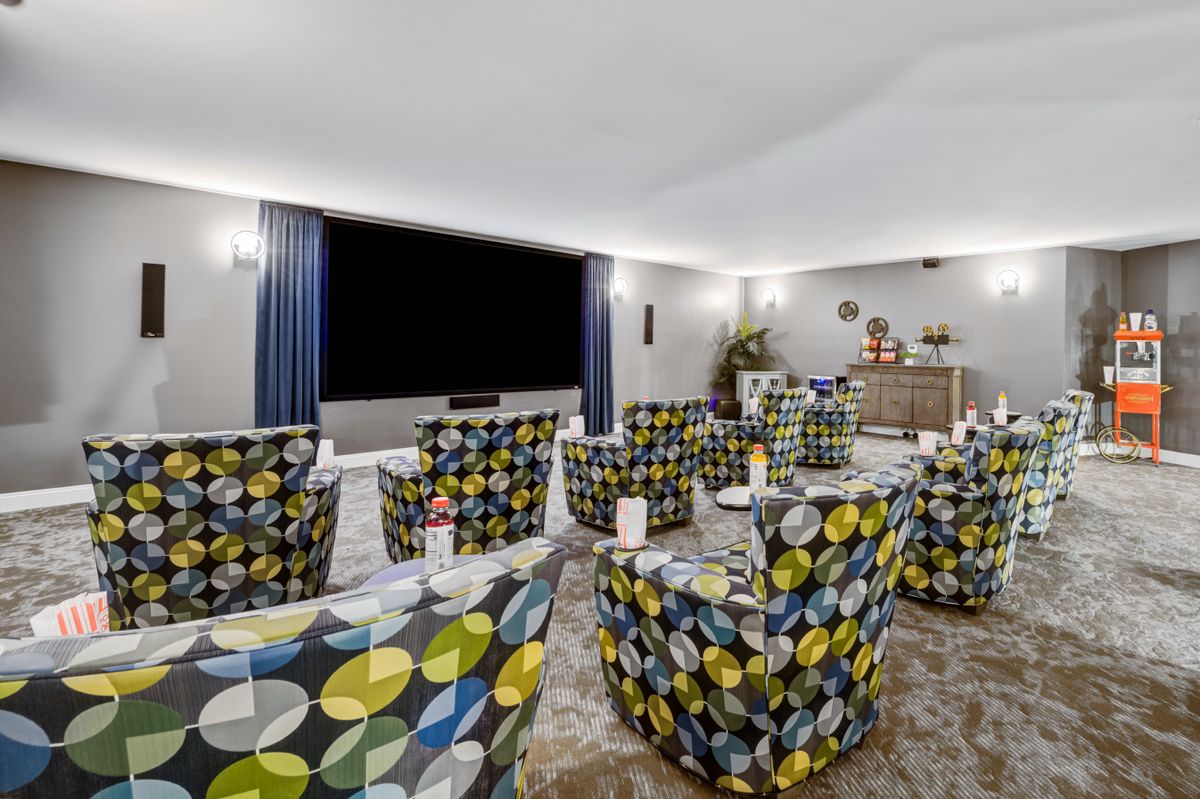 A modern home theater room with colorful patterned chairs facing a large screen.
