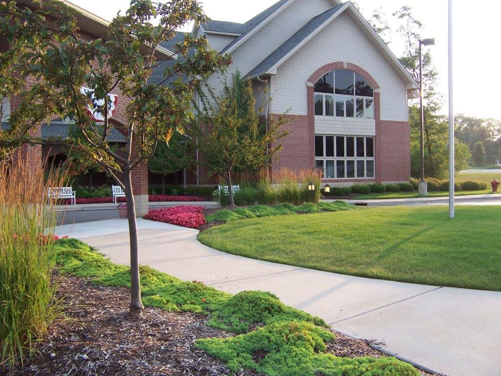 A well-maintained lawn and landscaped garden leading to a brick building with large windows.
