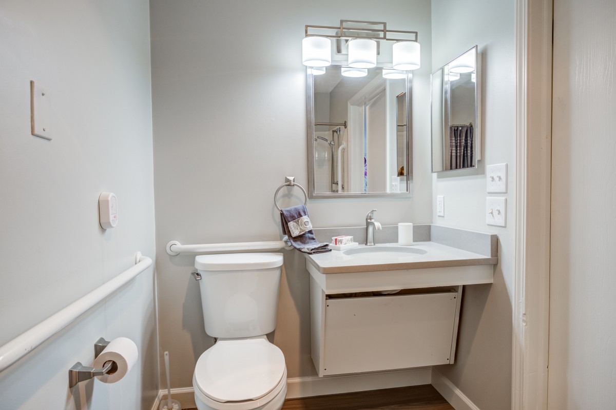 A modern bathroom with a toilet, sink, and mirror under stylish lighting.