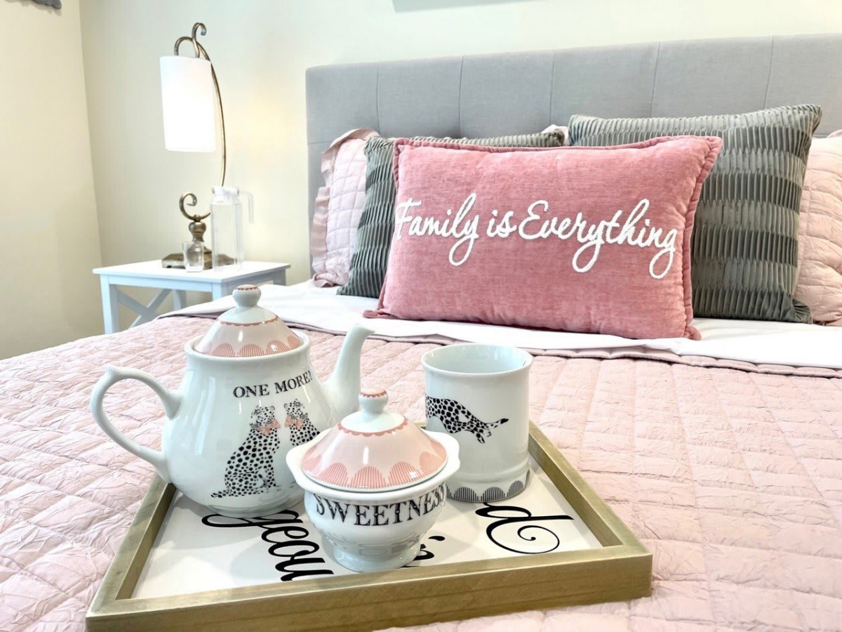 A cozy bedroom setup with a pink pillow and a tea set on a tray.