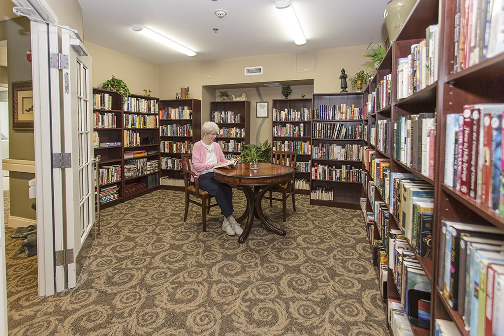 An elderly person reading in a cozy library room surrounded by bookshelves.