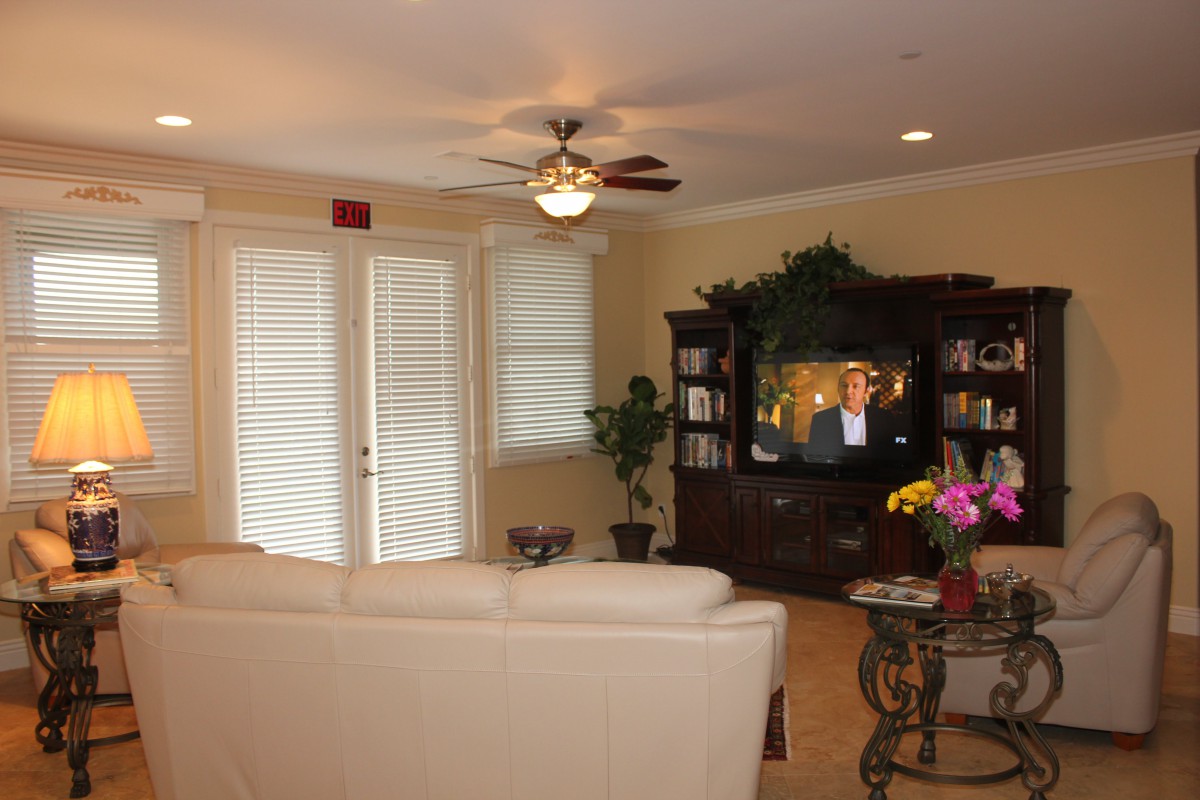 A cozy living room featuring a white sofa, television, ceiling fan, and elegant home decor.