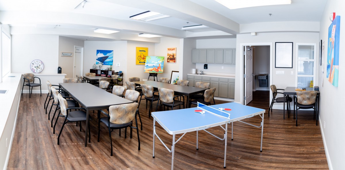 A community room featuring a meeting area with tables and chairs, along with a small ping pong table for recreation.