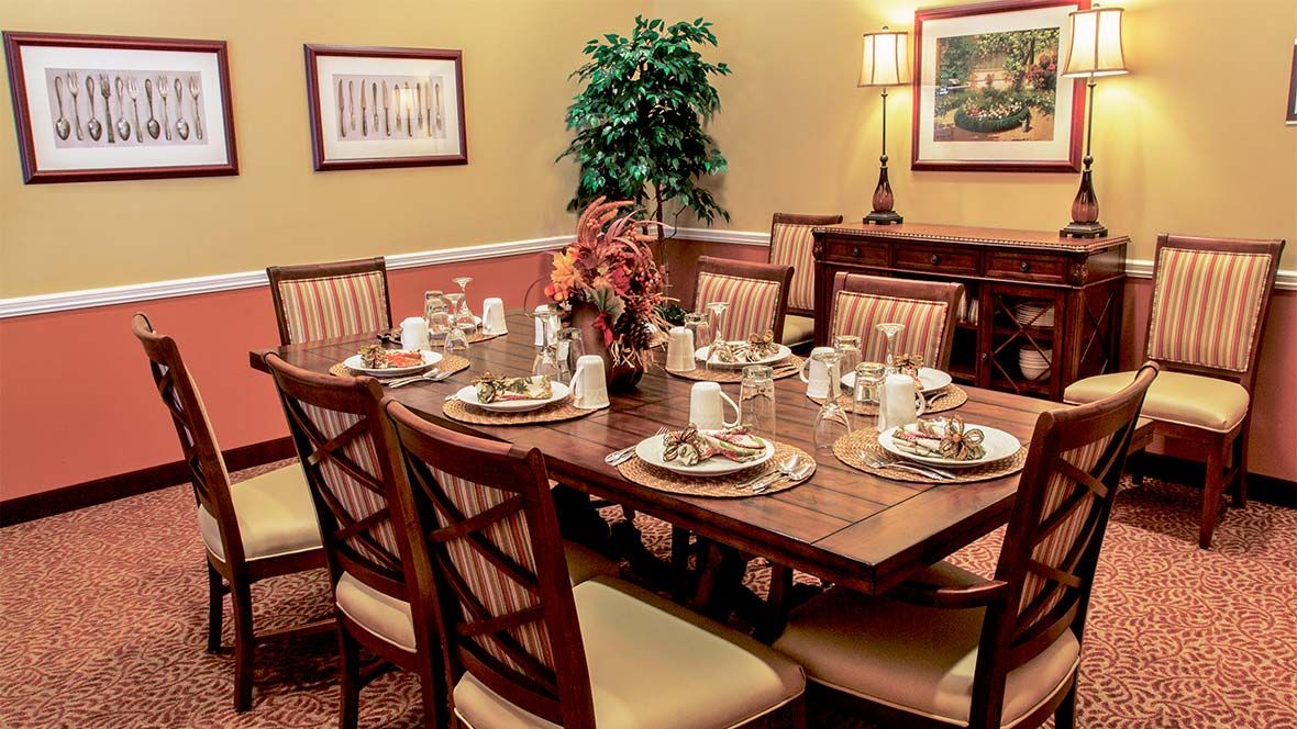An elegantly set dining table with neatly arranged plates and napkins, surrounded by cushioned chairs in a warmly decorated dining room.