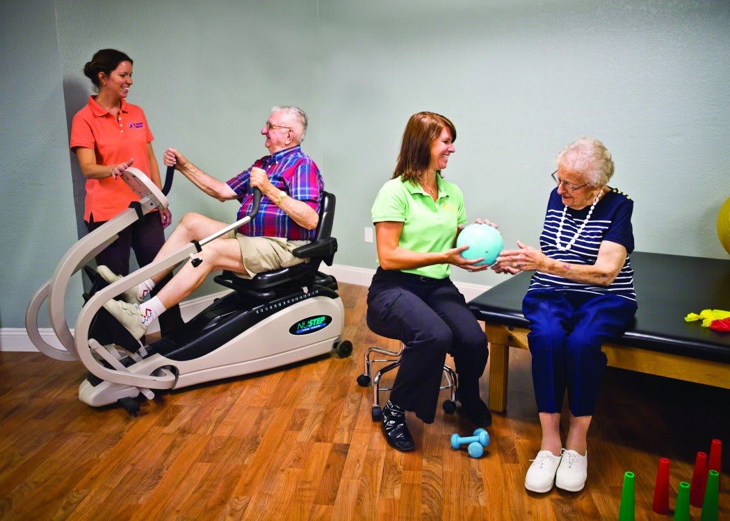 Elderly individuals participating in physical therapy exercises with the assistance of caregivers.