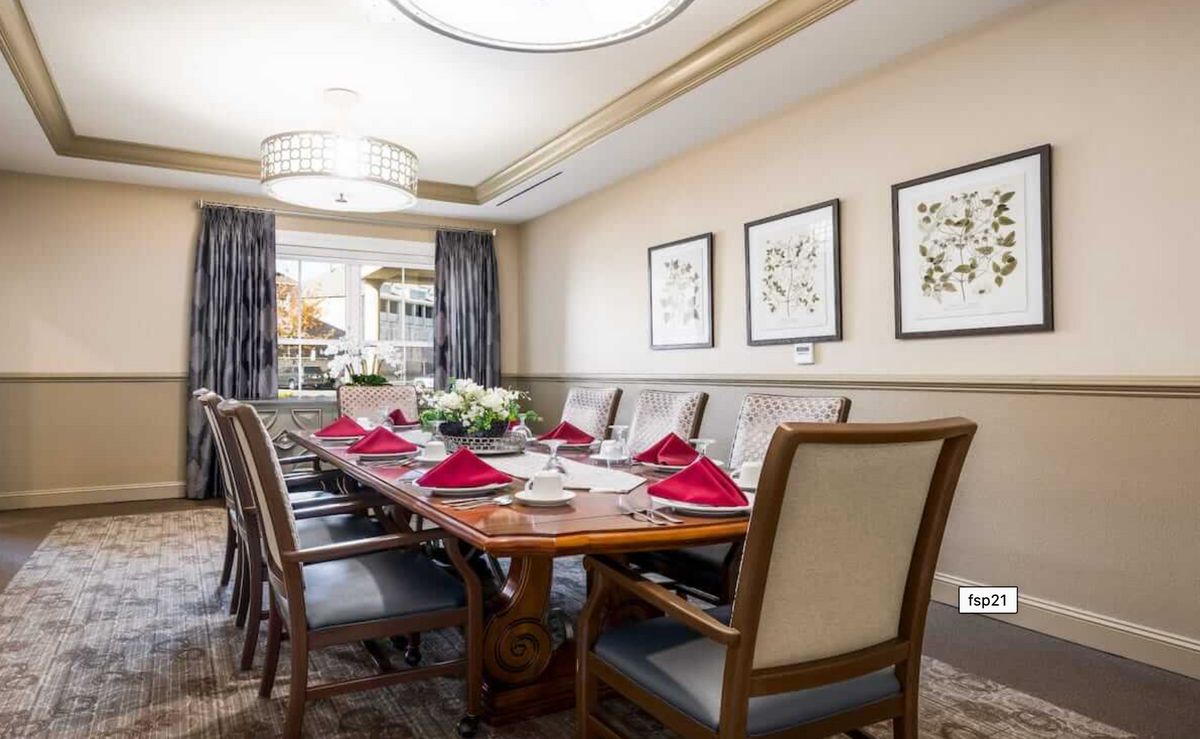 A well-decorated dining room with a large table set for dinner, featuring red napkins and floral centerpieces.