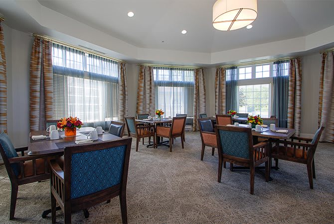 A well-lit dining room with multiple tables and chairs, featuring large windows and elegant decor.
