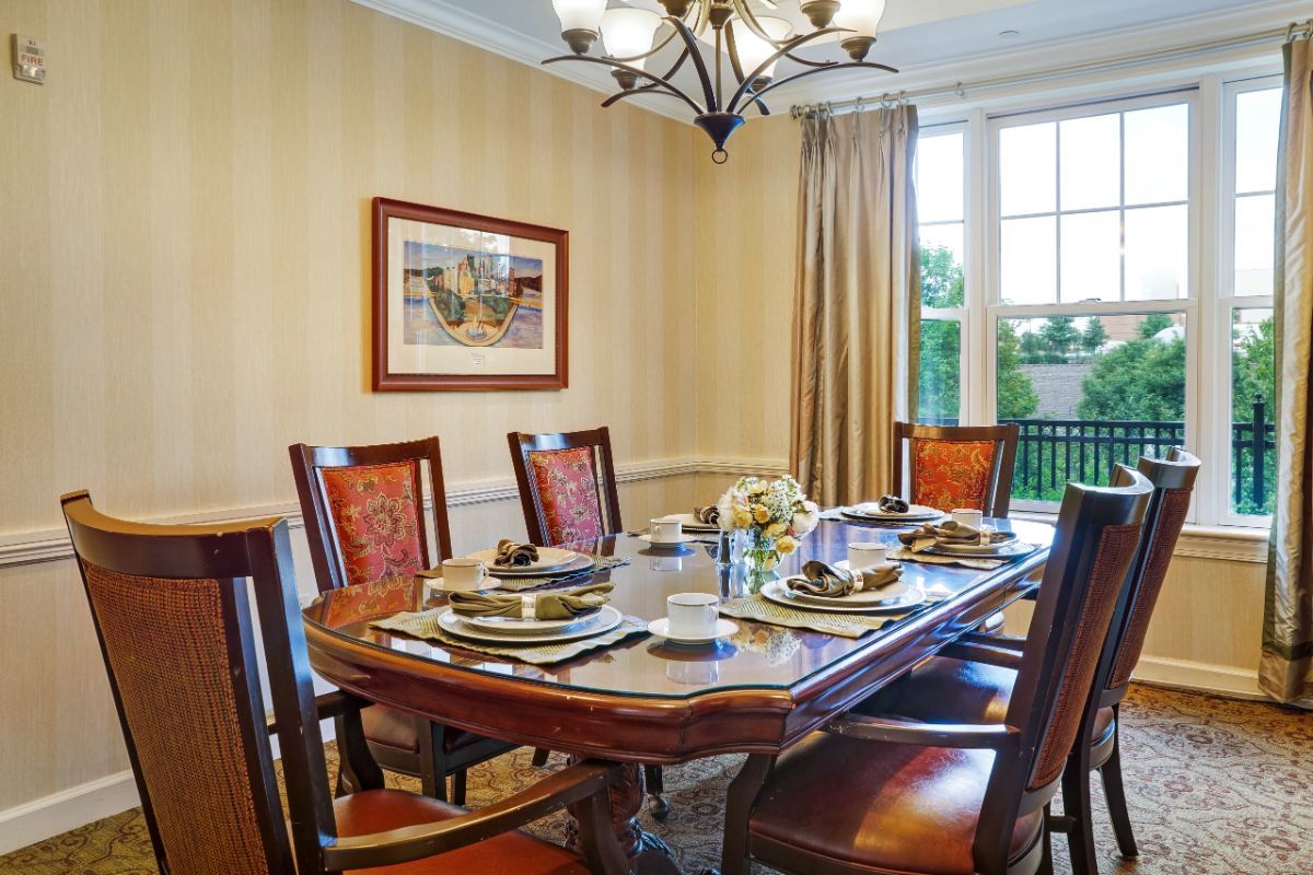 A well-decorated dining room featuring a wooden table set with plates and utensils, surrounded by chairs under an elegant chandelier.